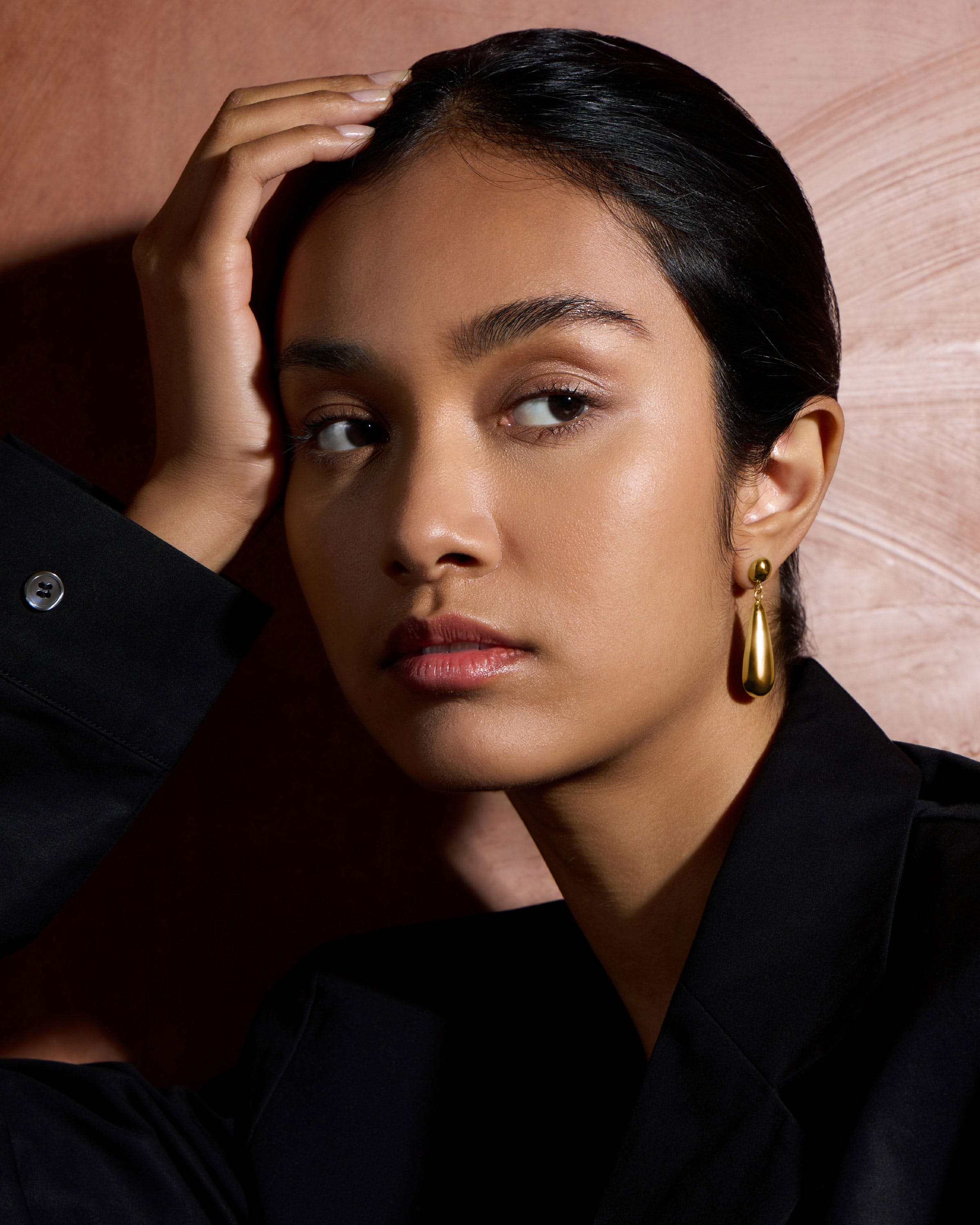 Close-up portrait of woman wearing 24-carat gold gilded teardrop earrings and black blazer.