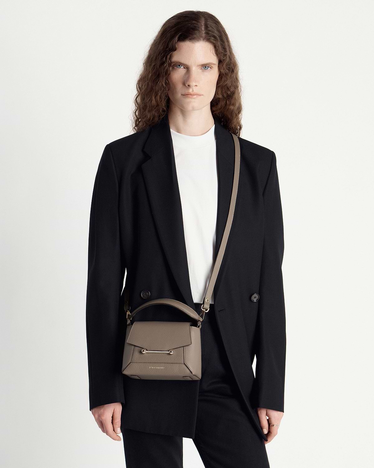 Model wearing taupe Strathberry Mosaic Nano bag with top handle and crossbody strap.