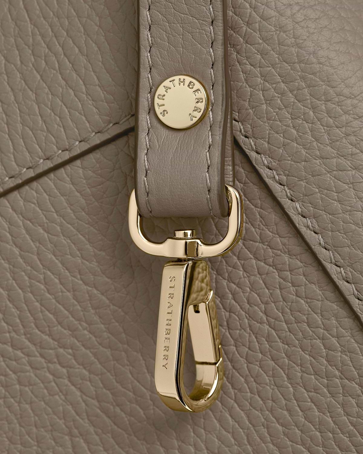 Taupe pebbled leather with gold Strathberry clasp and strap hardware detail.