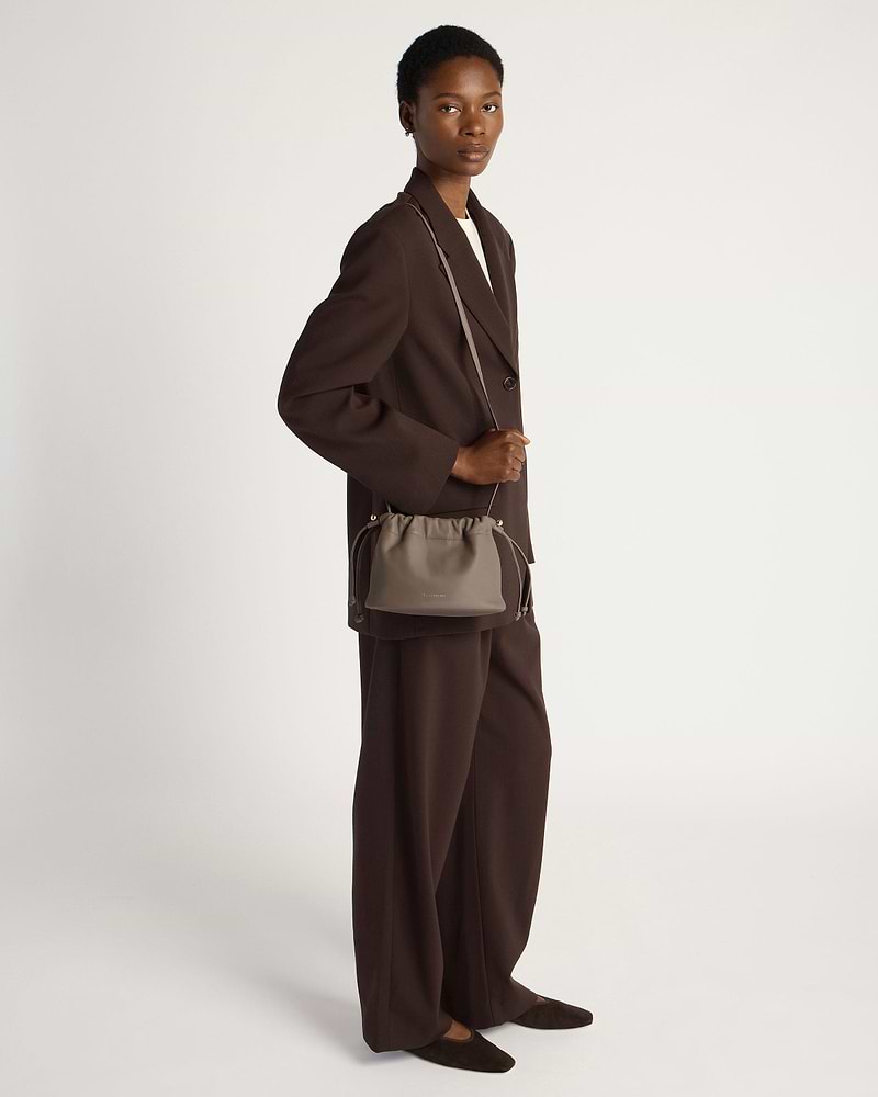 Model in dark brown suit carrying a taupe drawstring cross-body bag.