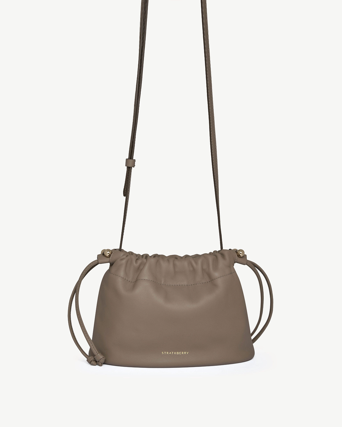 Taupe leather drawstring bag with adjustable shoulder strap and gold Strathberry logo.