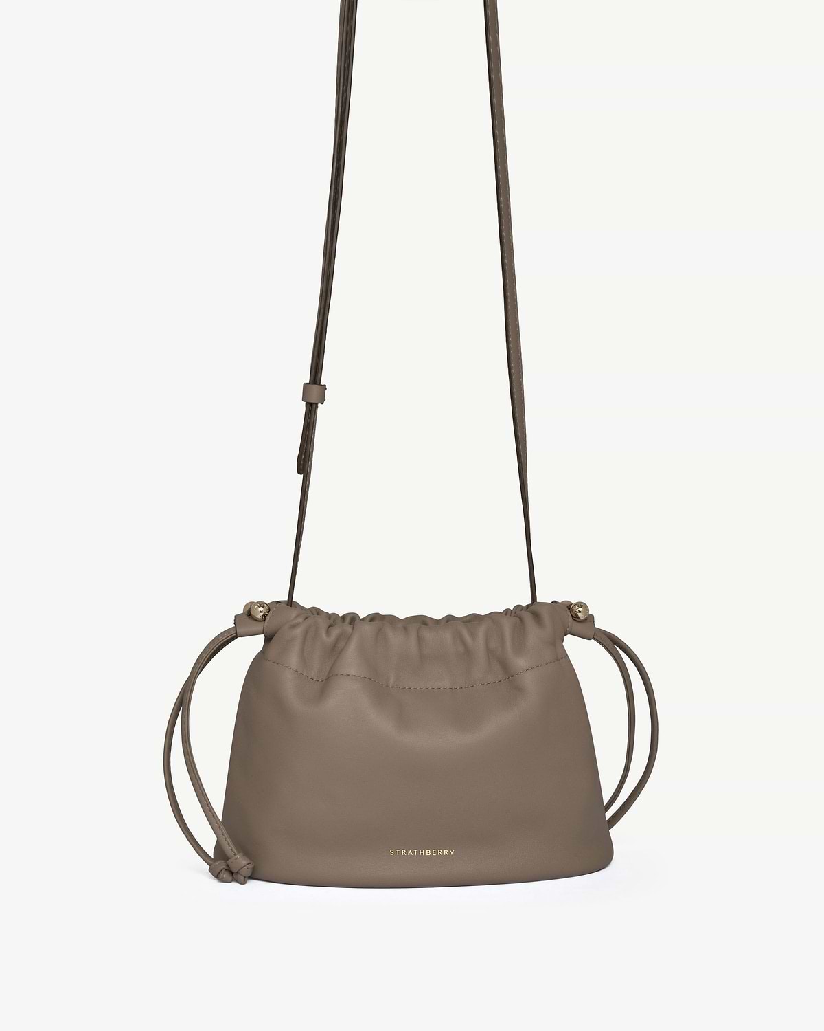 Taupe leather drawstring bag with adjustable shoulder strap and gold Strathberry logo.