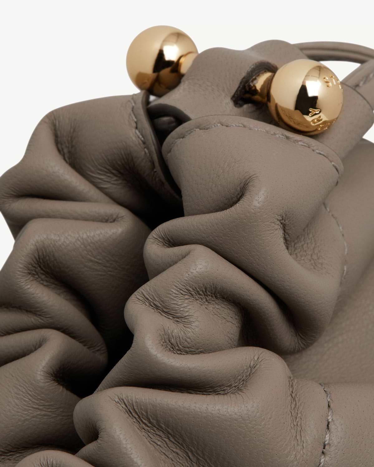 Close-up of taupe leather drawstring bag with gold ball hardware.