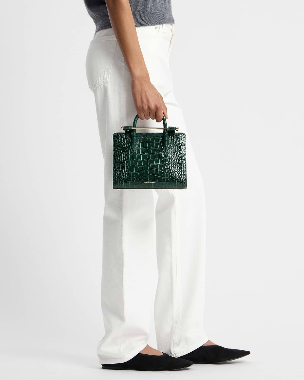 Hand holding green croc mini tote with gold bar handle and Strathberry logo.