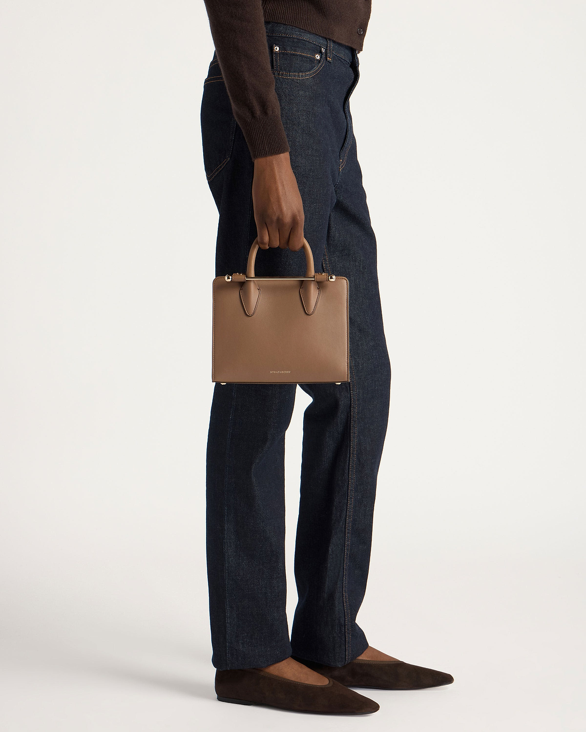 Model waist-down holding Strathberry clay mini tote by top handles.