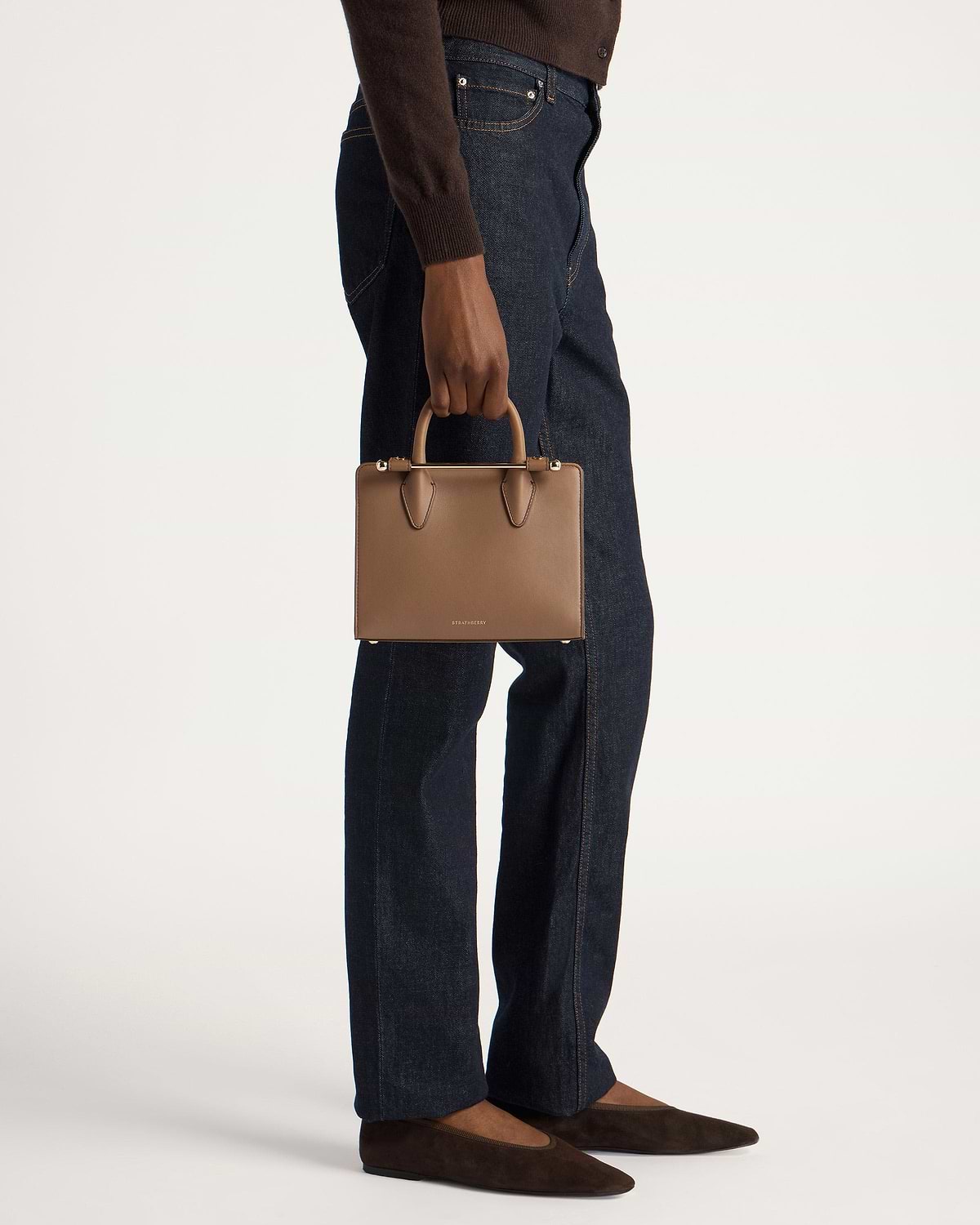 Model waist-down holding Strathberry clay mini tote by top handles.