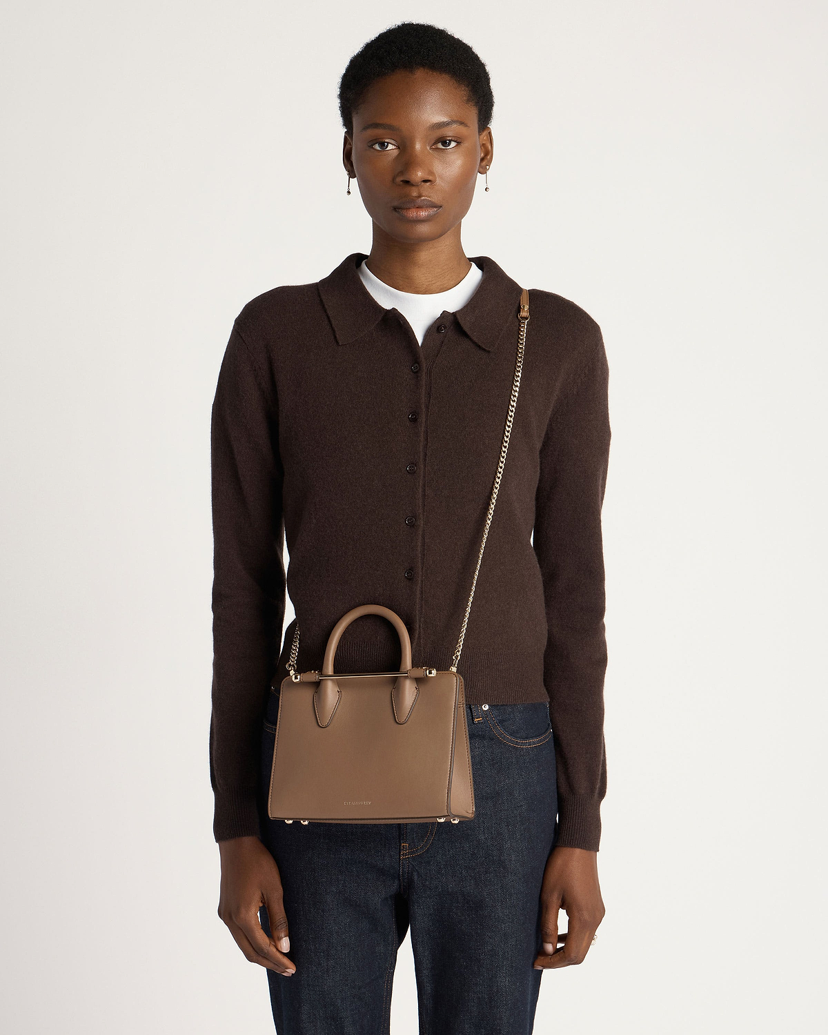 Model wearing dark brown cardigan carrying clay mini tote with chain shoulder strap.