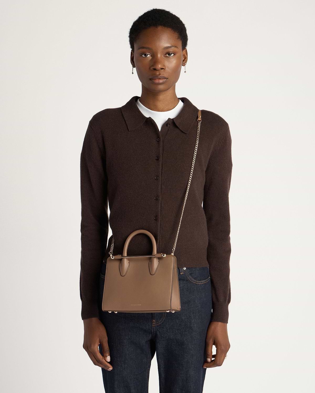 Model wearing dark brown cardigan carrying clay mini tote with chain shoulder strap.