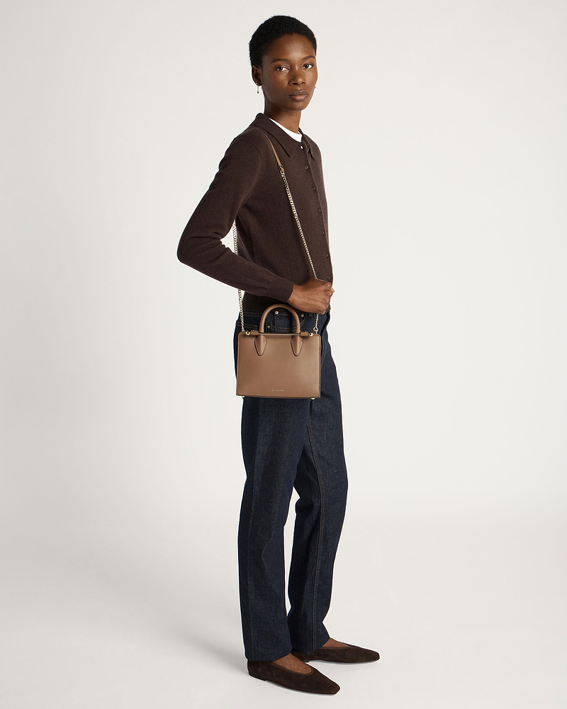 Model wearing dark brown cardigan and jeans holds clay mini tote with chain strap.