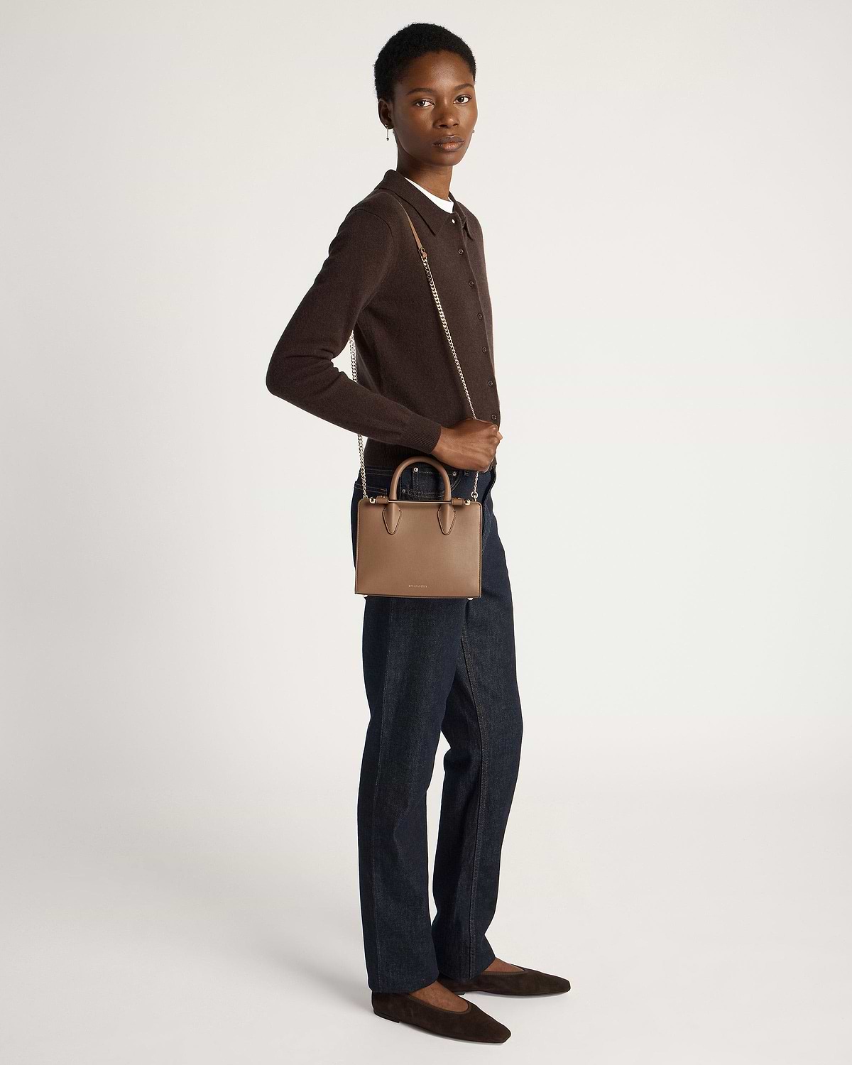 Model wearing dark brown cardigan and jeans holds clay mini tote with chain strap.