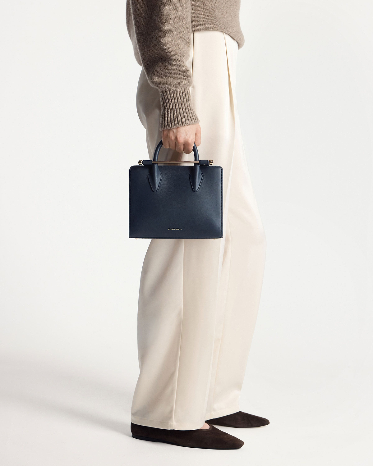 Model holding marine blue Strathberry mini tote by top handles, side view