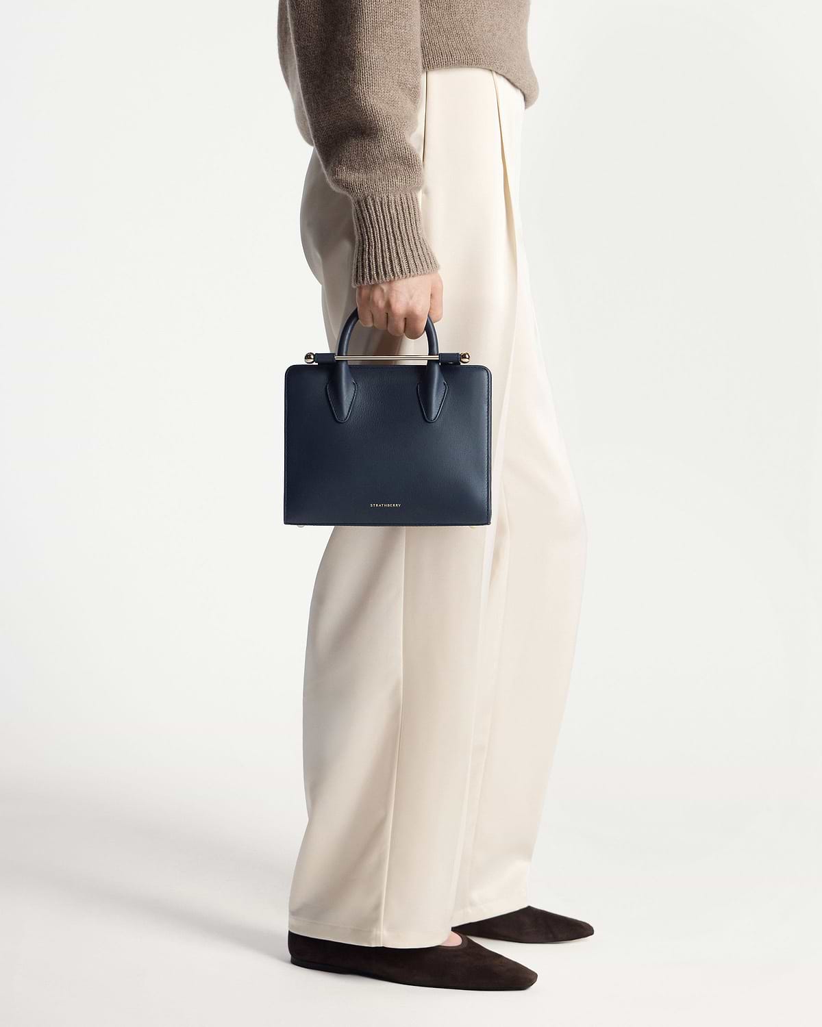 Model holding marine blue Strathberry mini tote by top handles, side view