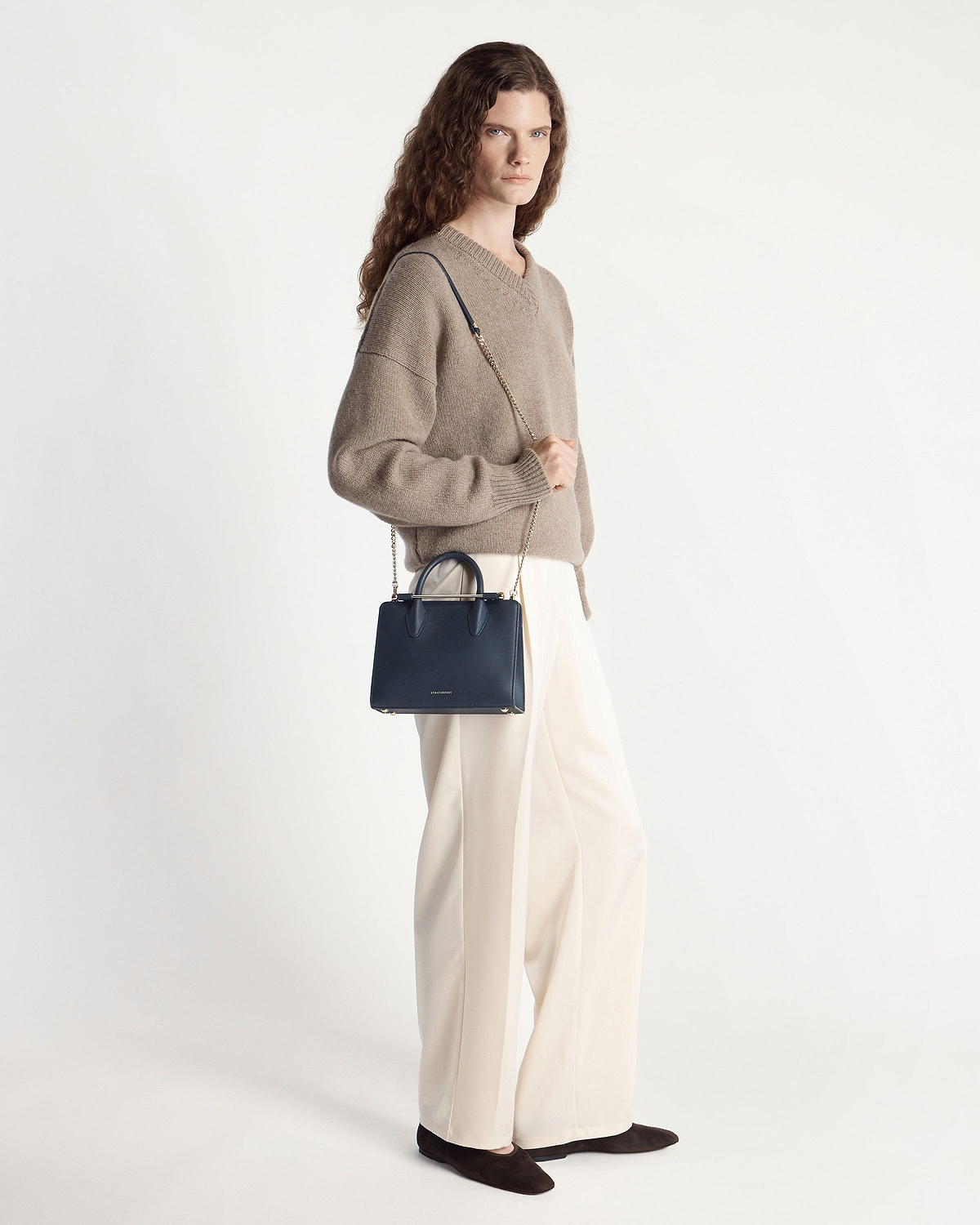 Model wearing beige sweater and cream trousers holding marine blue Strathberry mini tote