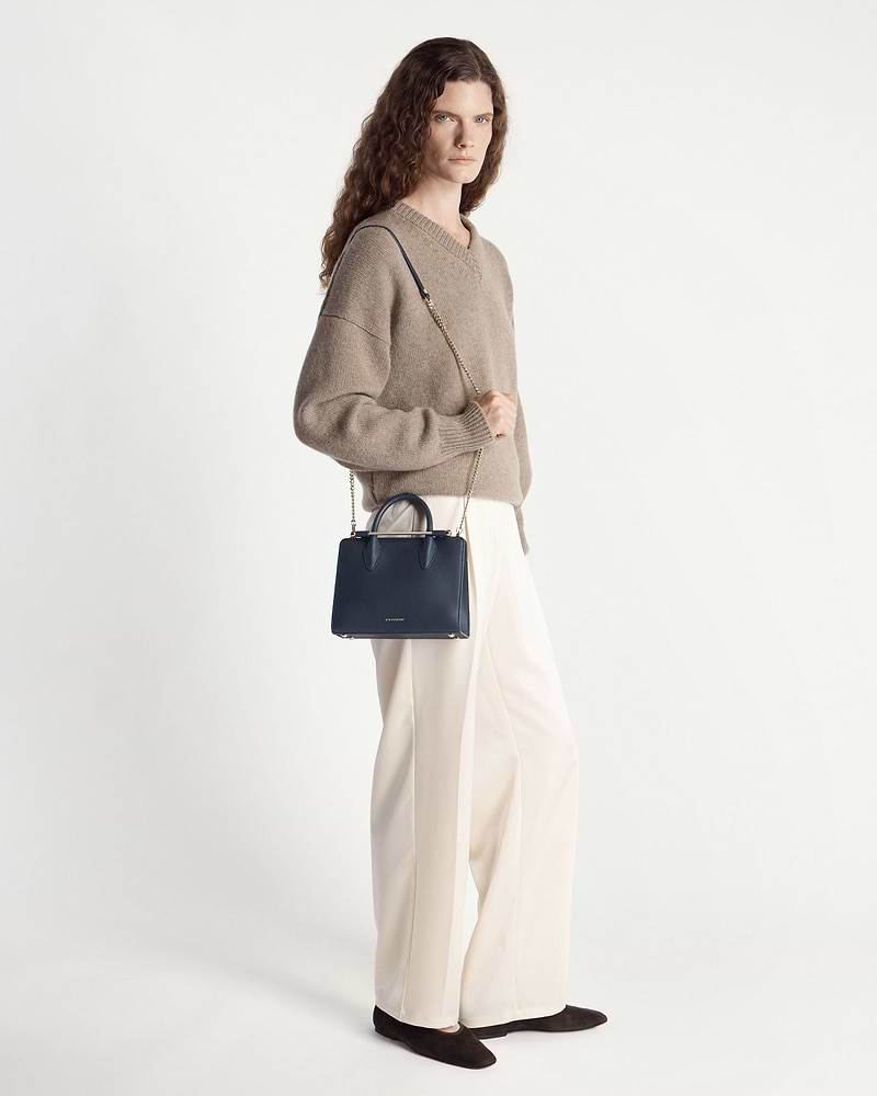 Model wearing beige sweater and cream trousers holding marine blue Strathberry mini tote