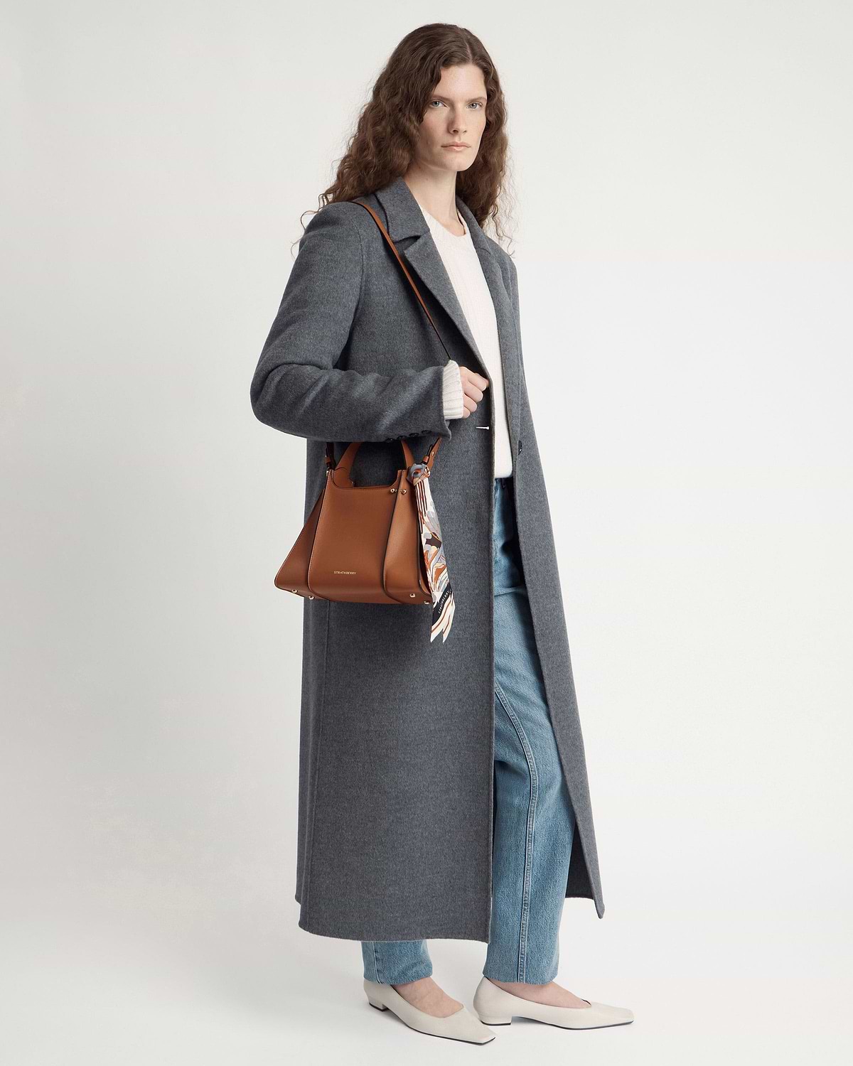 Model wearing tan Arkshell shoulder bag with patterned silk scarf and long grey coat.