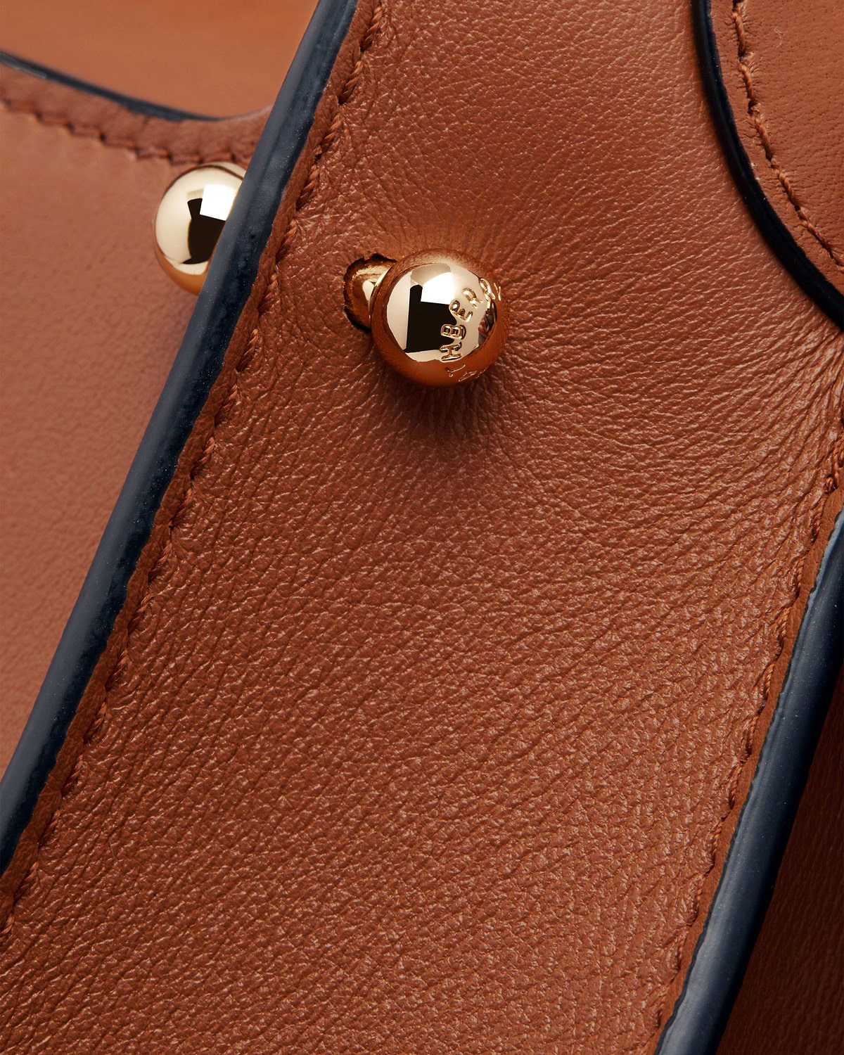 Tan Arkshell leather close-up showing gold stud, dark edge trim and stitching
