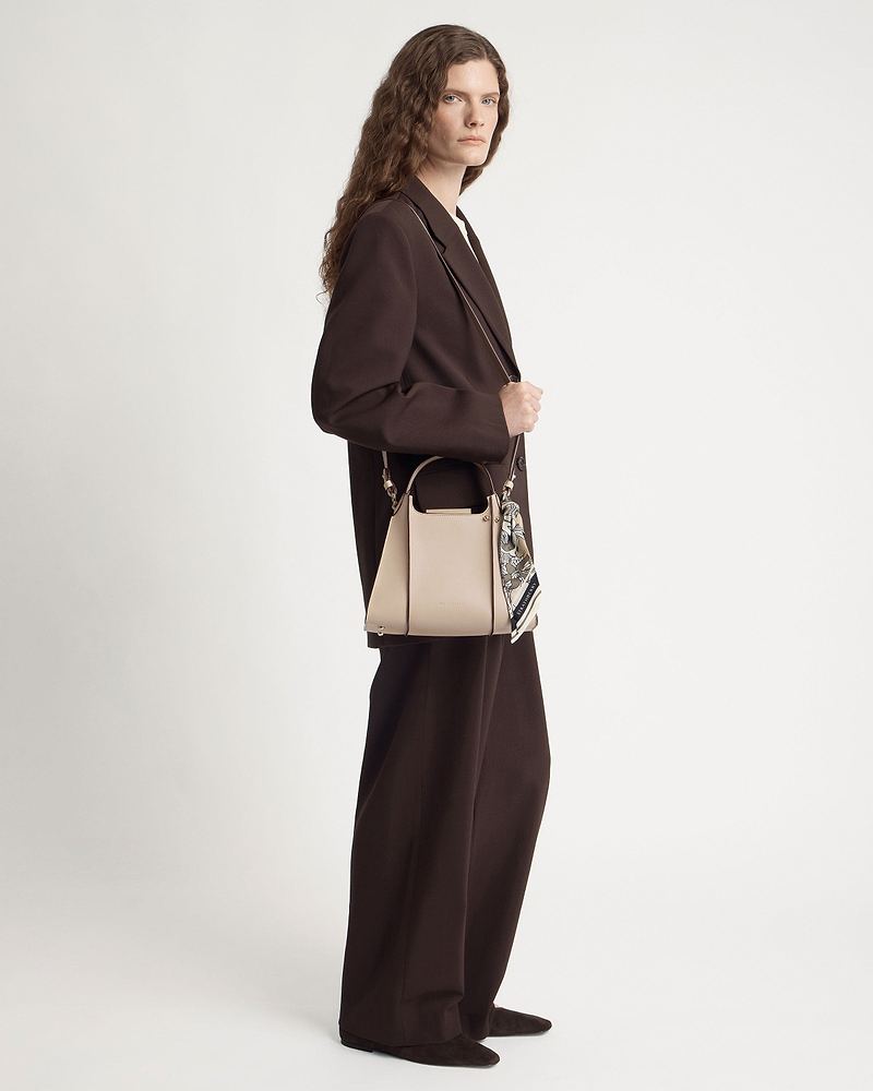 Model in brown suit holding an oat-coloured structured leather handbag with silk scarf.