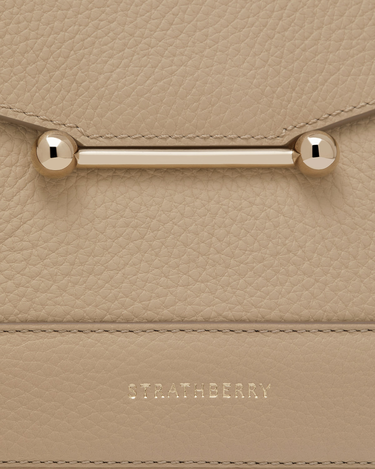 Close-up of sand mosaic bag leather, gold bar clasp and Strathberry logo.