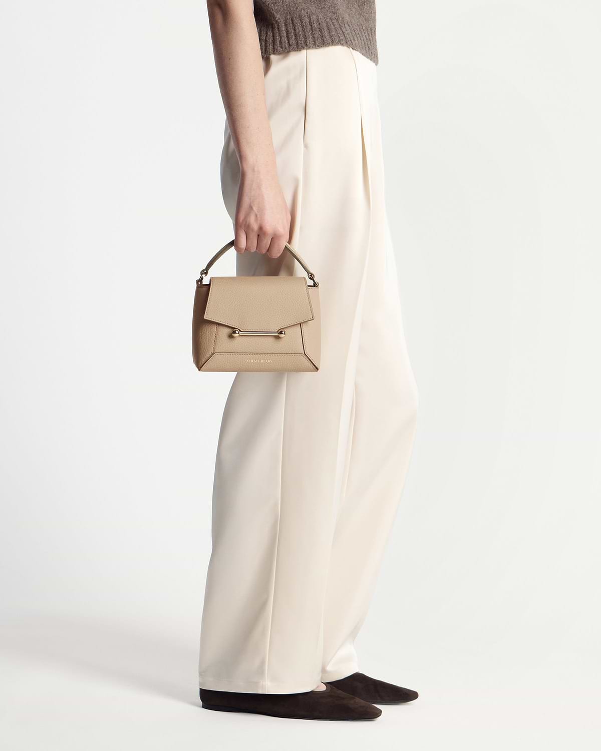 Model's waist and hand holding a Strathberry Mosaic Nano bag in sand.