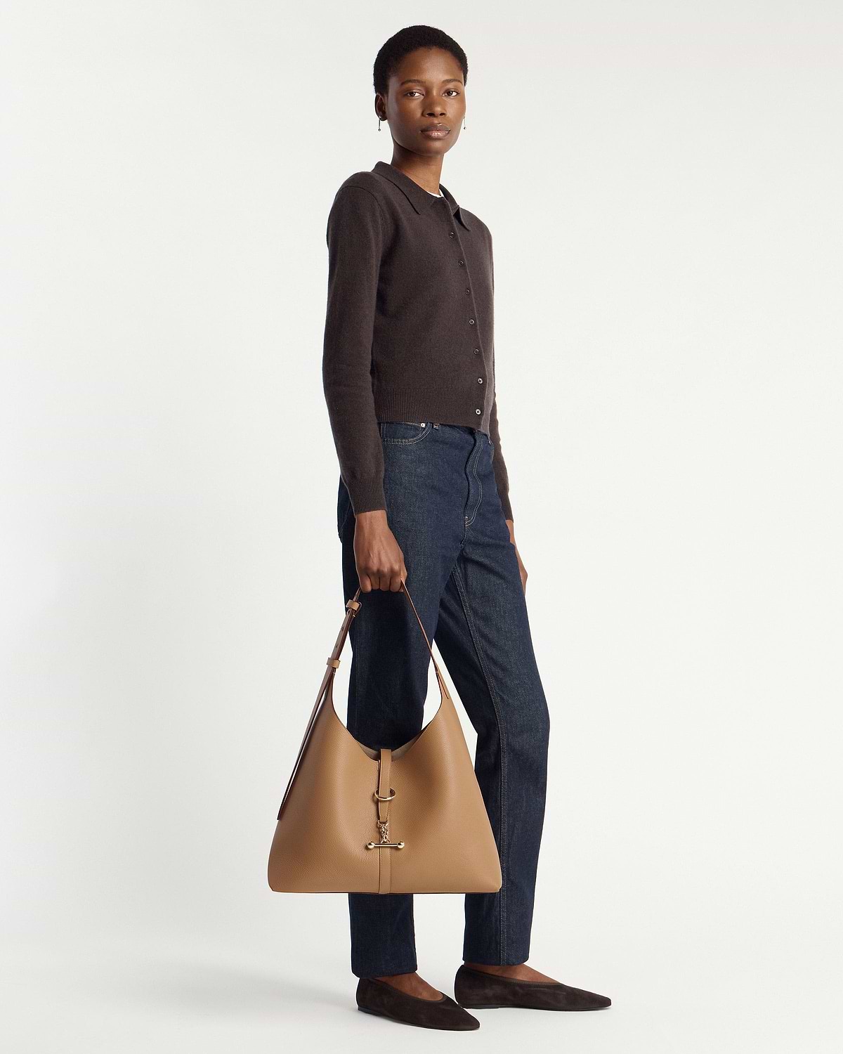 Model holding a caramel hobo bag with gold hardware, wearing cardigan and jeans.