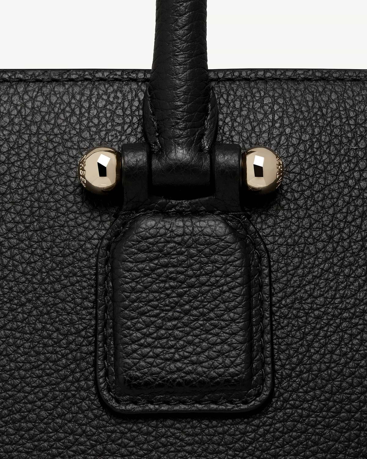Close-up of black pebbled leather bag handle attachment with two gold studs.