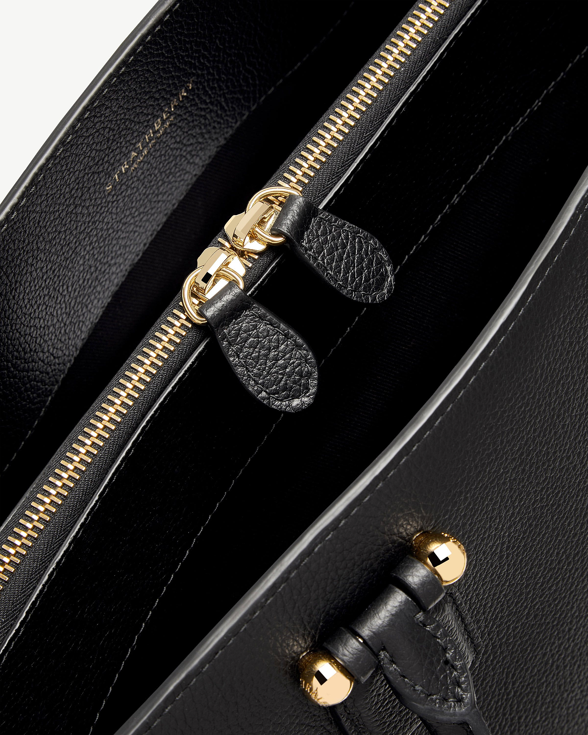 Close-up of black Strathberry bag interior showing gold zip and leather pull tabs.