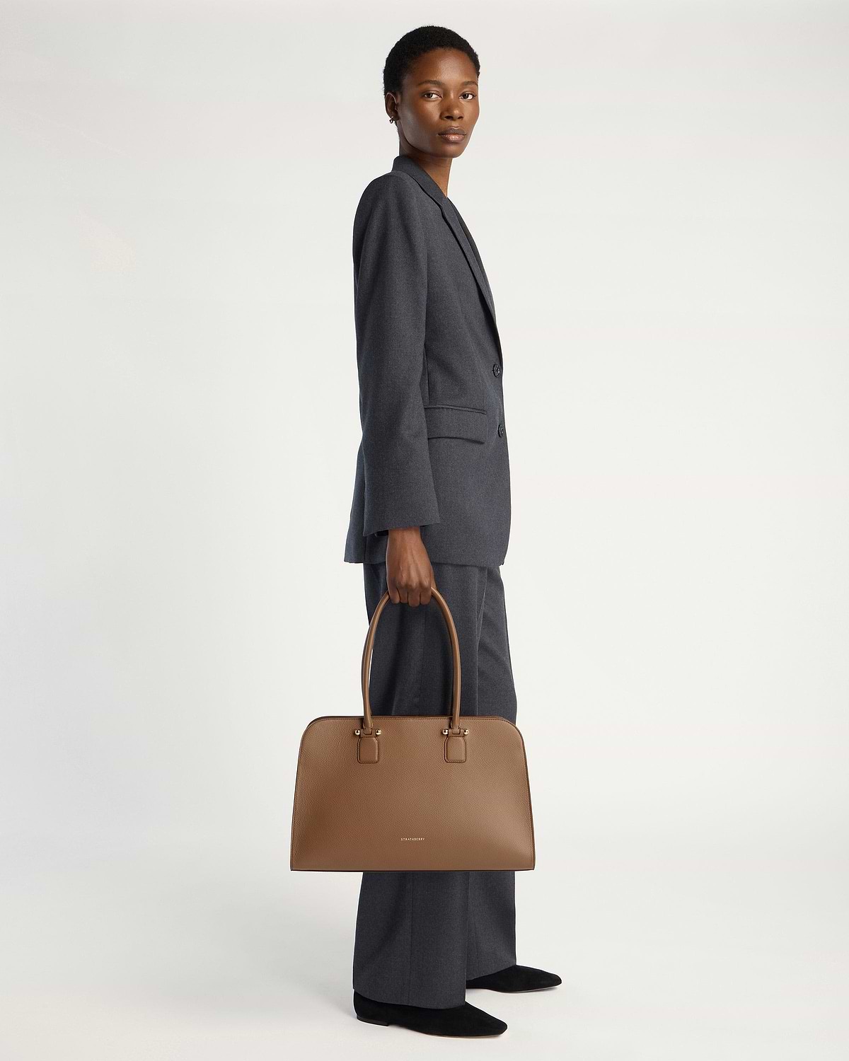 Model holding clay Georgia Maxi handbag by Strathberry, full-length view.