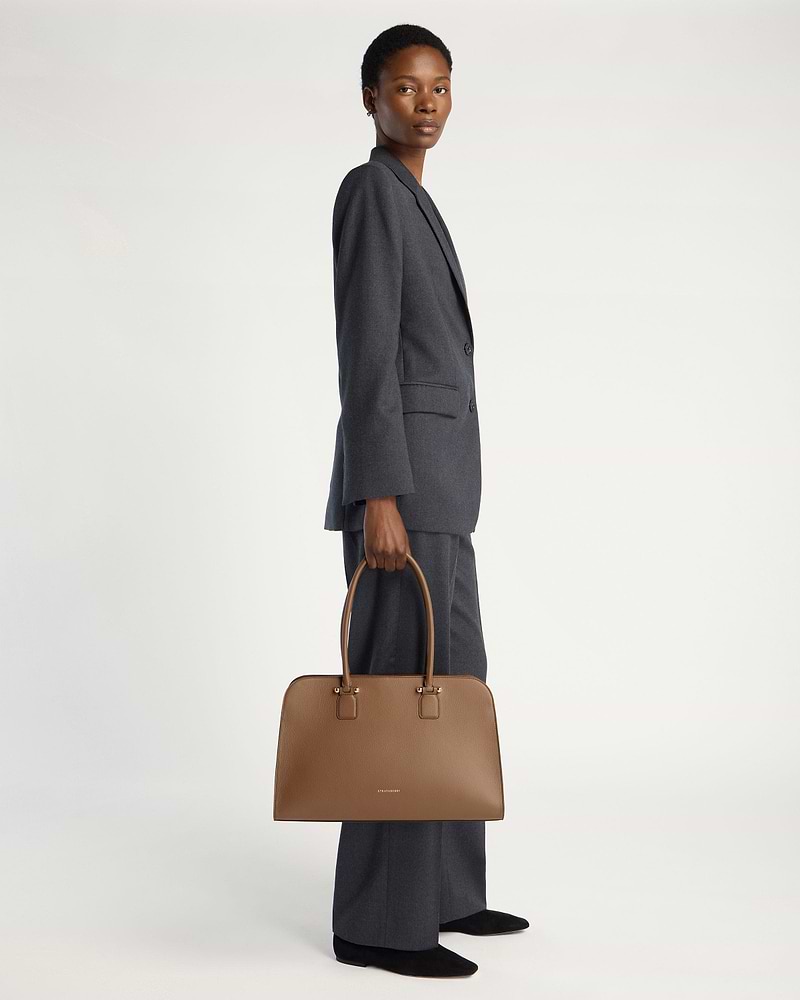 Model holding clay Georgia Maxi handbag by Strathberry, full-length view.