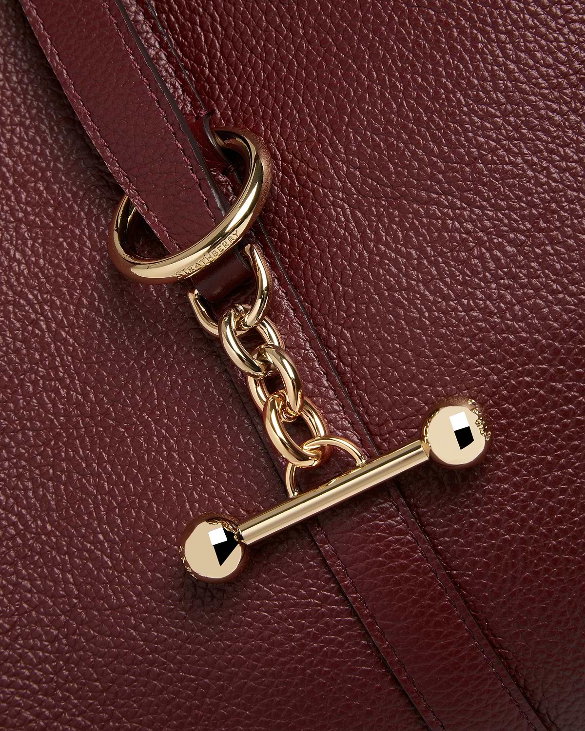 Oxblood pebbled leather strap with gold chain hardware and Strathberry logo.