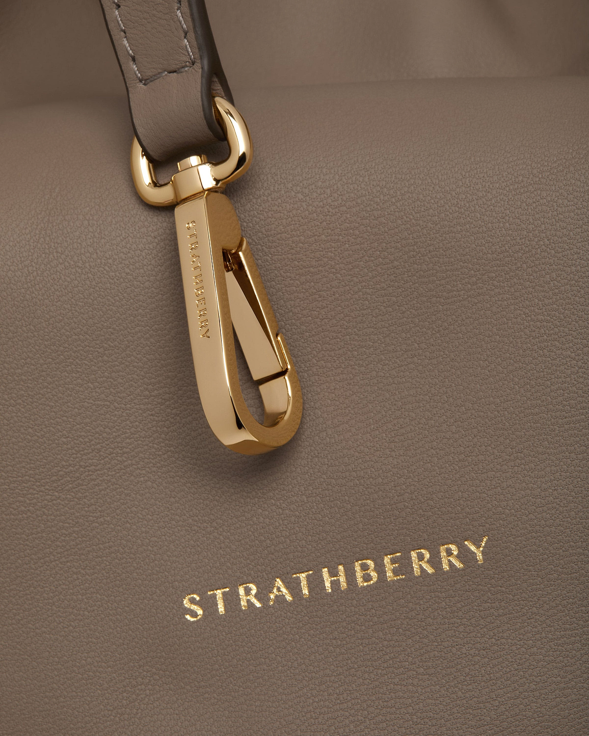 Taupe leather Charlotte Midi drawstring bag with engraved gold clasp and Strathberry logo.