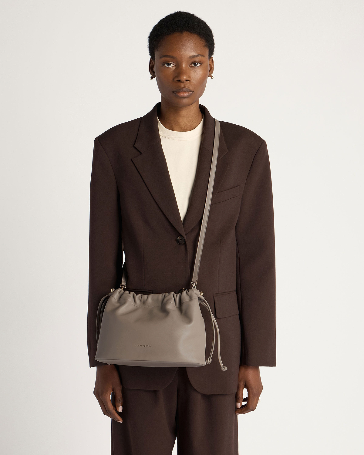 Model wearing taupe Charlotte Midi drawstring bag with long shoulder strap.
