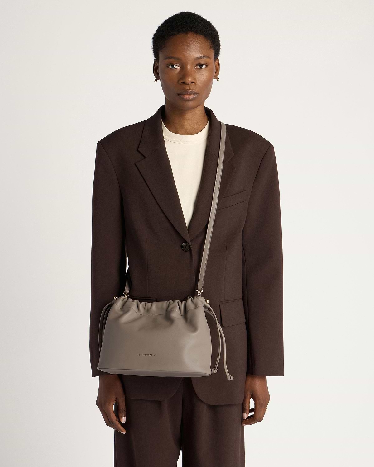 Model wearing taupe Charlotte Midi drawstring bag with long shoulder strap.