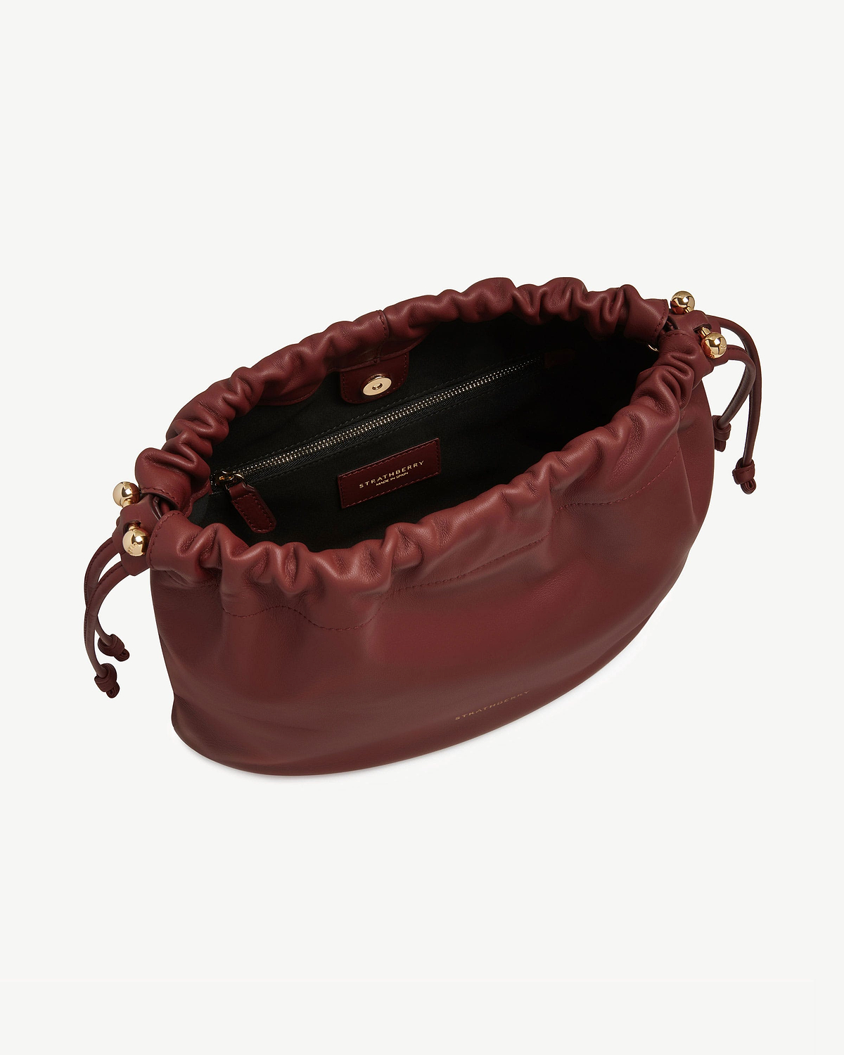Strathberry oxblood Charlotte midi drawstring bag open, showing interior zip pocket and gold hardware.