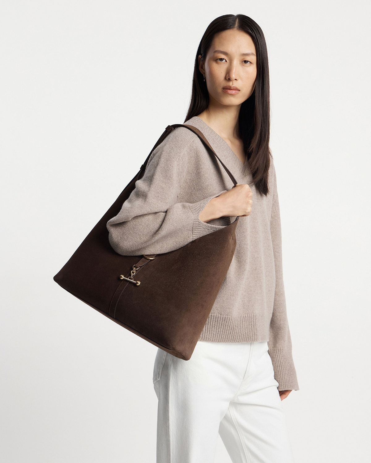 Model carrying chocolate suede Kite Hobo Maxi shoulder bag with gold clasp.