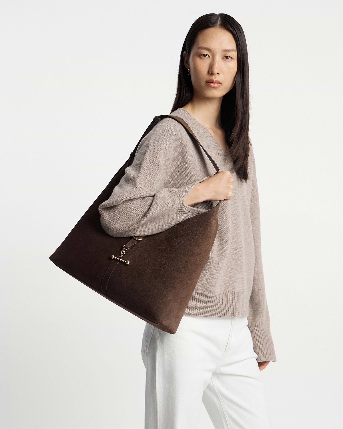 Model carrying chocolate suede Kite Hobo Maxi shoulder bag with gold clasp.