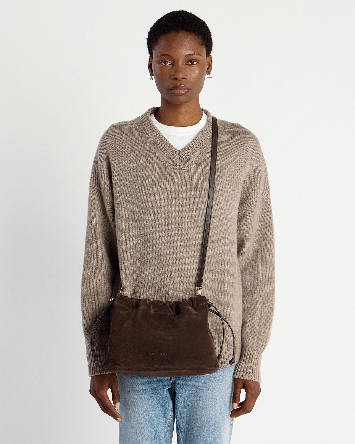 Woman wearing chocolate suede Charlotte Midi drawstring crossbody bag over knitted jumper