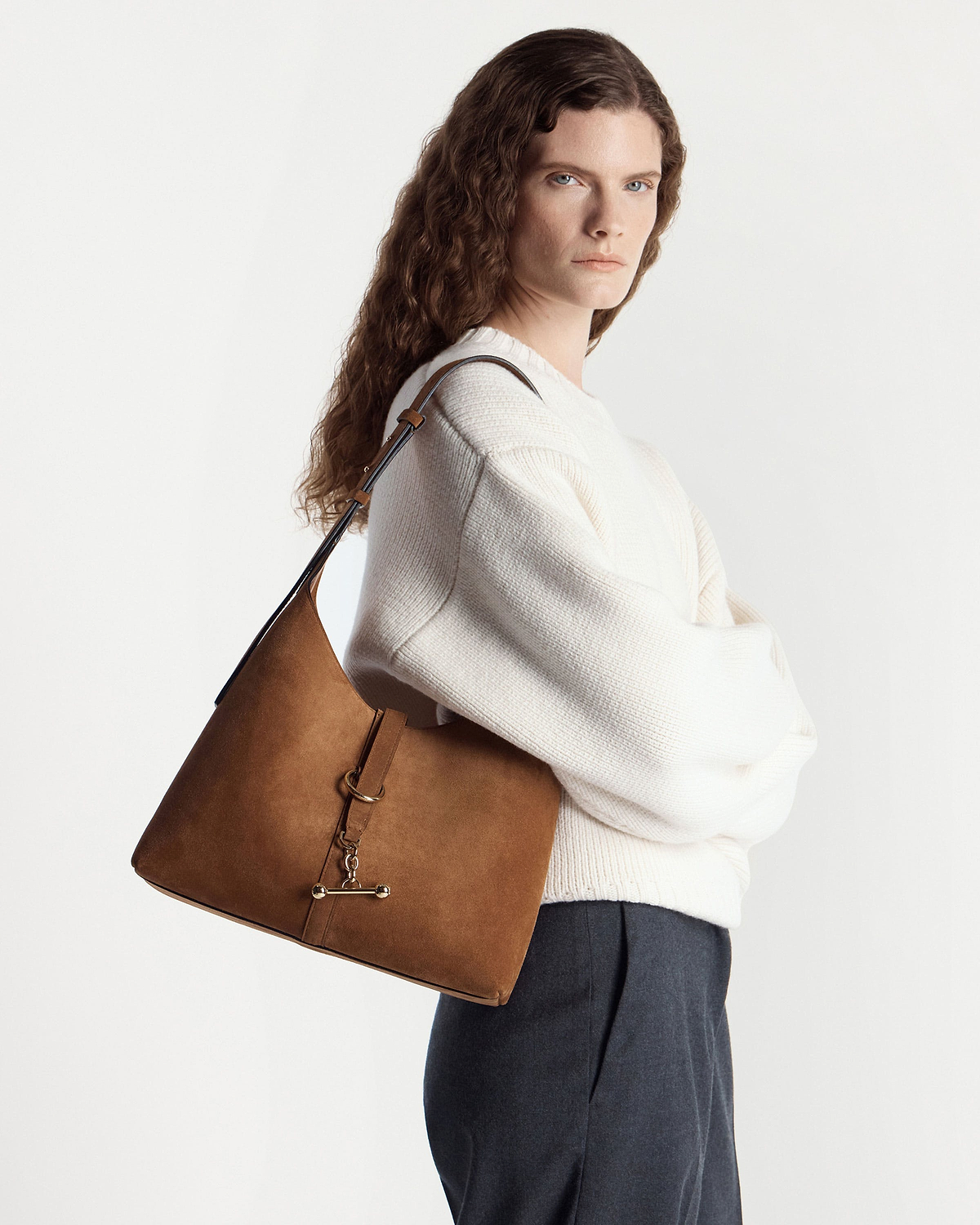 Woman in cream jumper carrying tan suede Kite Hobo bag on her shoulder