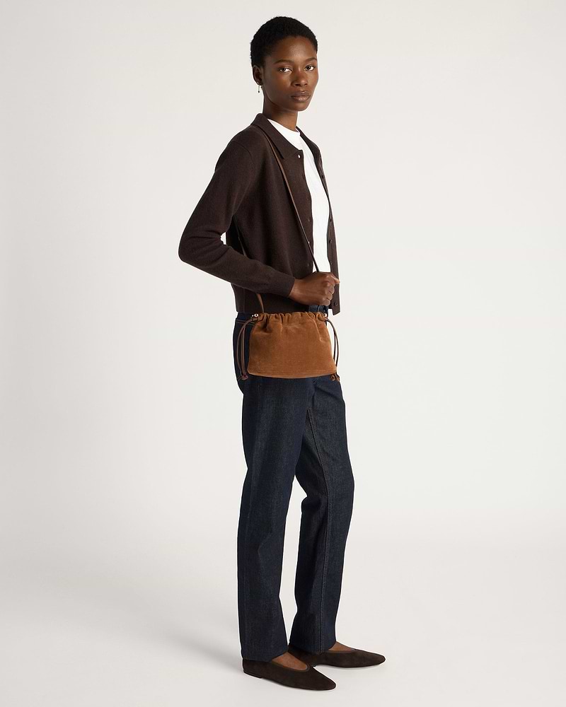 Model wearing tan suede drawstring bag across body with brown cardigan and dark jeans.