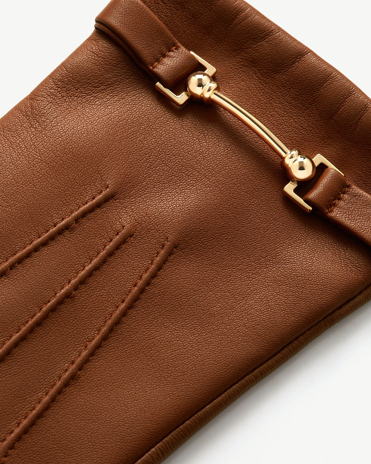 Detail of tan leather glove showing gold bar hardware and stitched details.