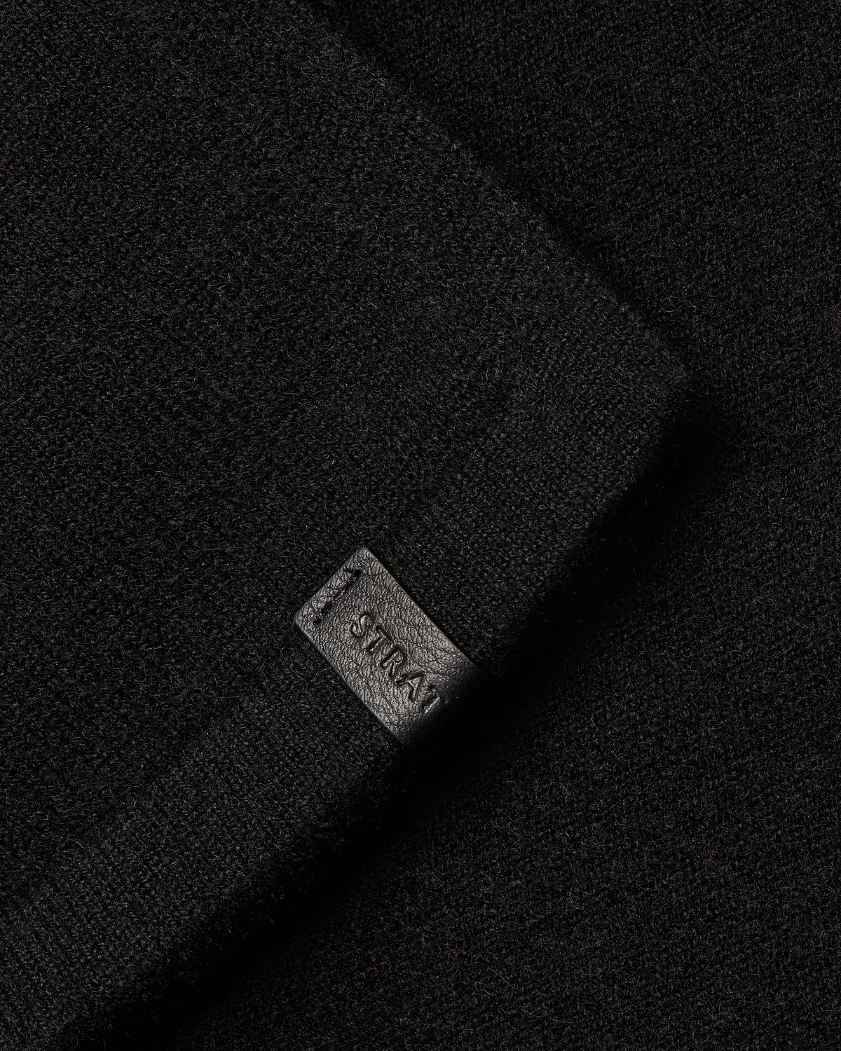 Black cashmere travel wrap with small Strathberry embossed leather tag visible.