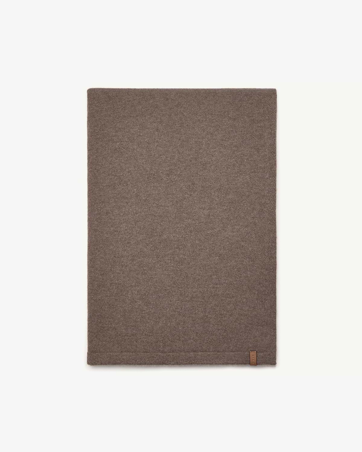 Otter-coloured cashmere travel wrap laid flat on white background with small leather tag.