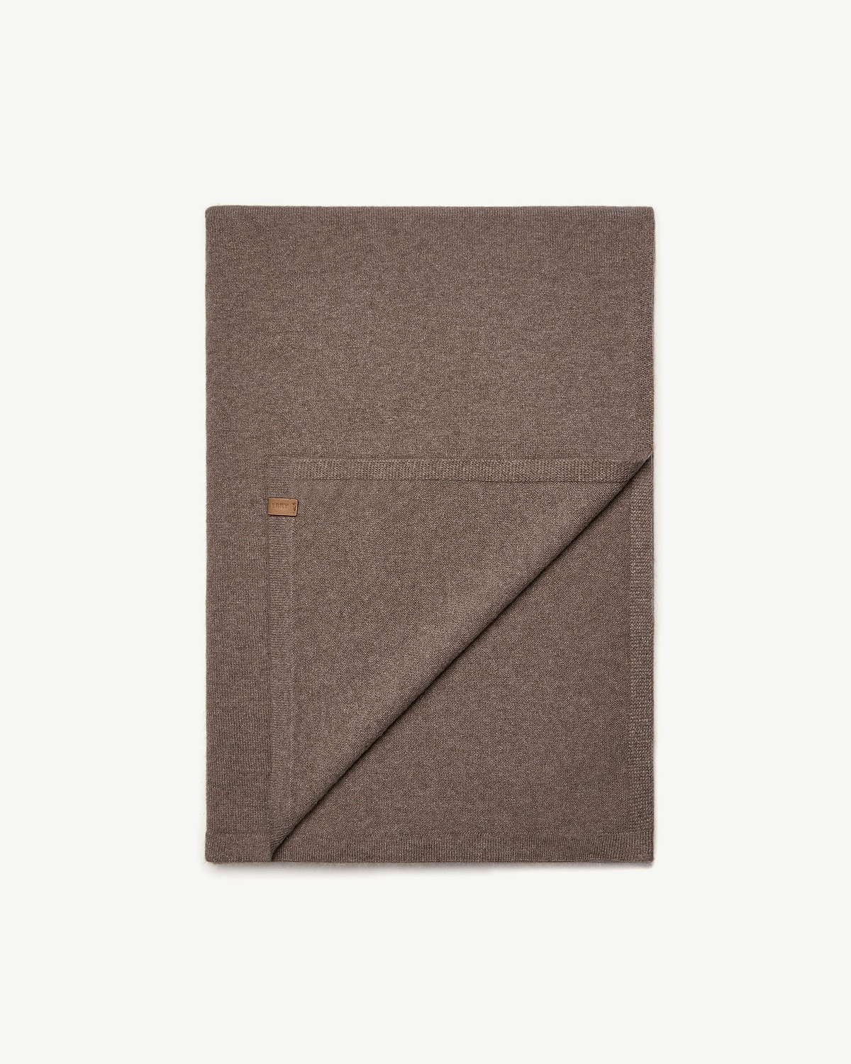 Folded otter brown cashmere travel wrap with small leather label on white background.