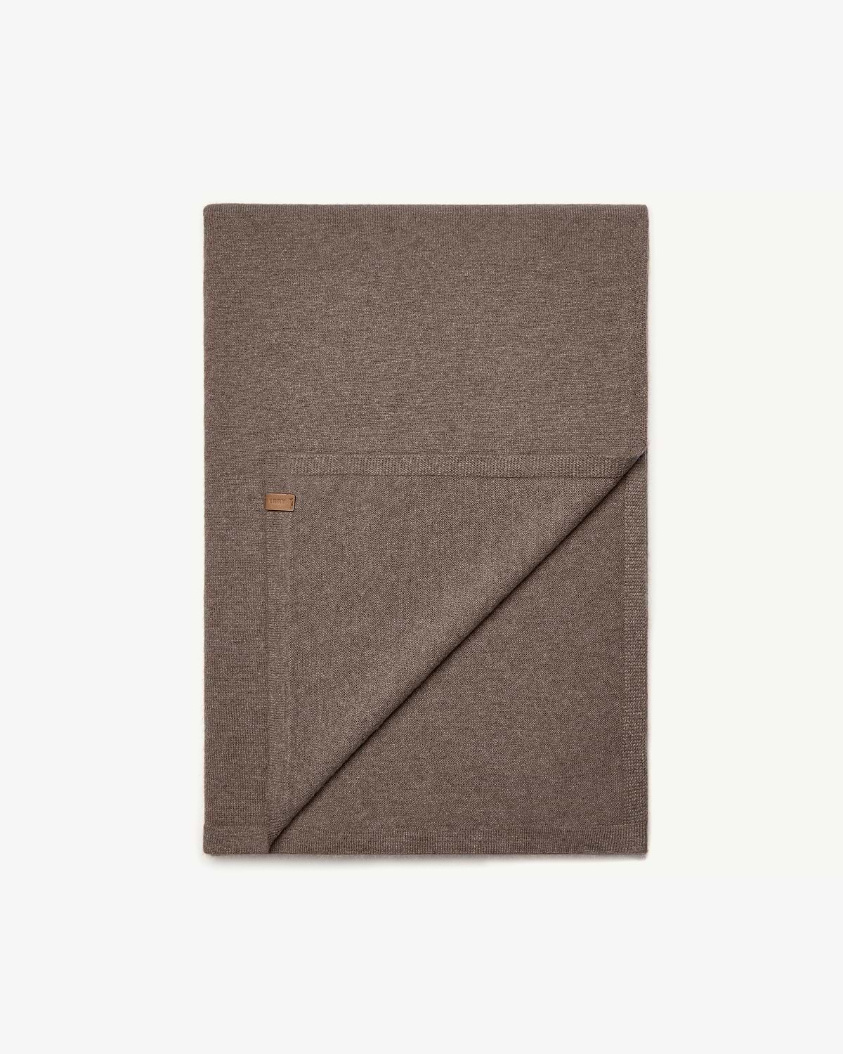 Folded otter brown cashmere travel wrap with small leather label on white background.
