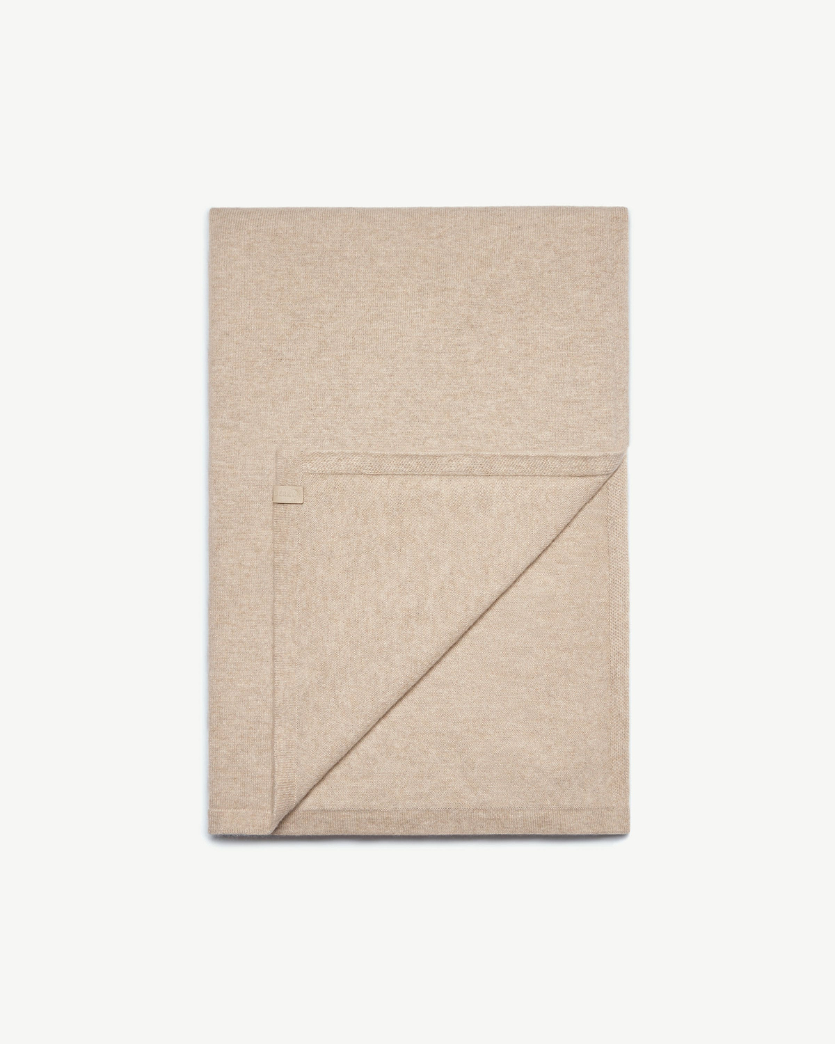 Folded oat-coloured cashmere travel wrap with a stitched corner tag and folded edge