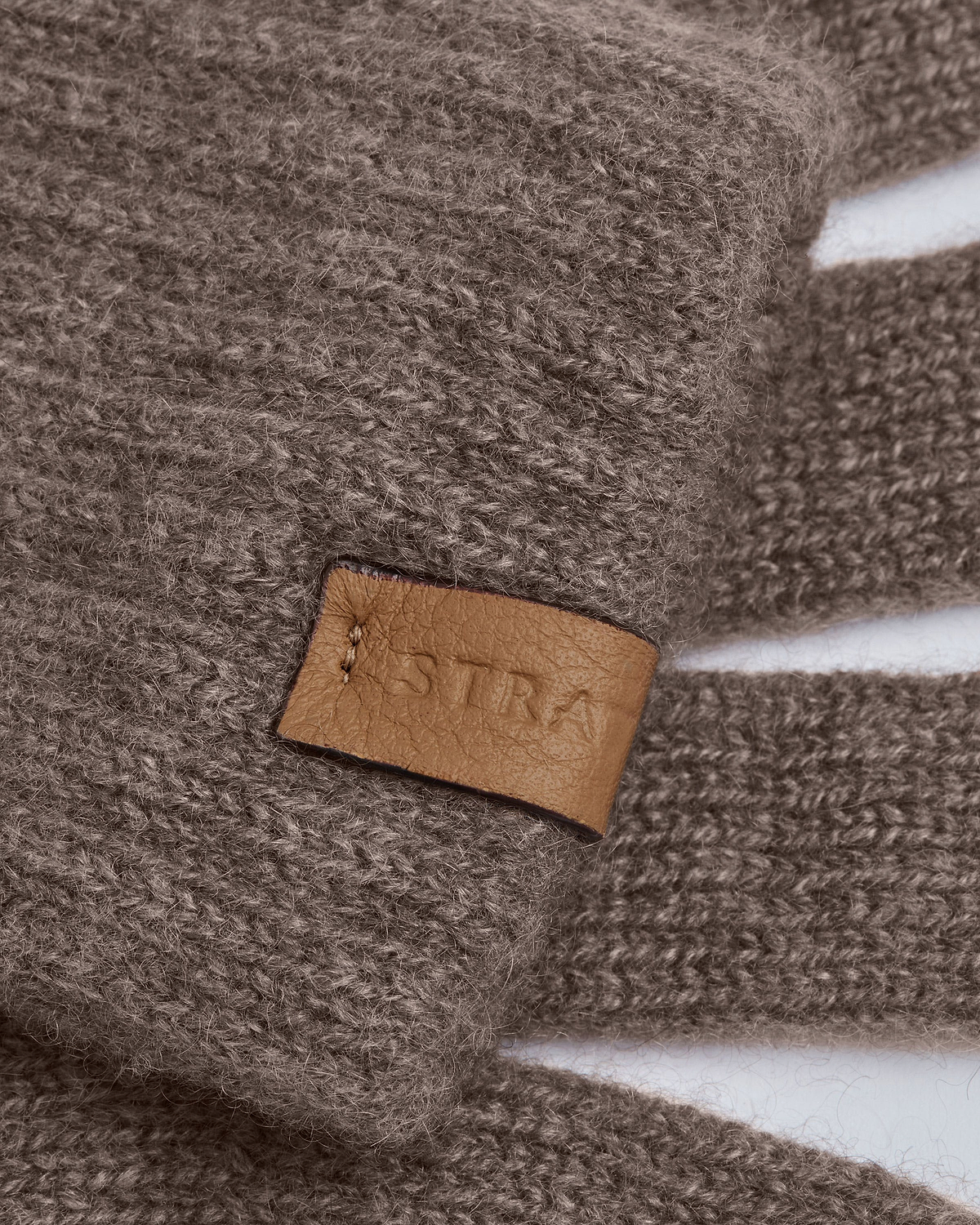 Close-up of otter-colour cashmere Westray gloves showing leather Strathberry label.