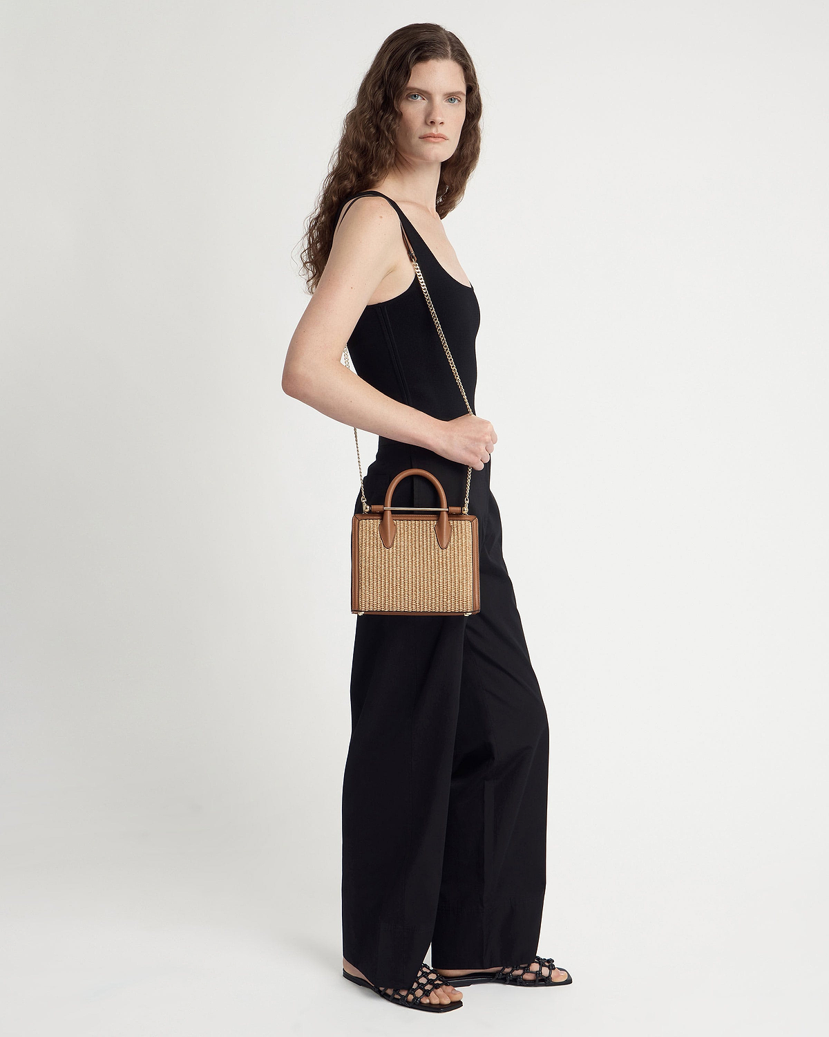 Woman in black outfit carrying tan raffia mini tote with leather trim and chain strap