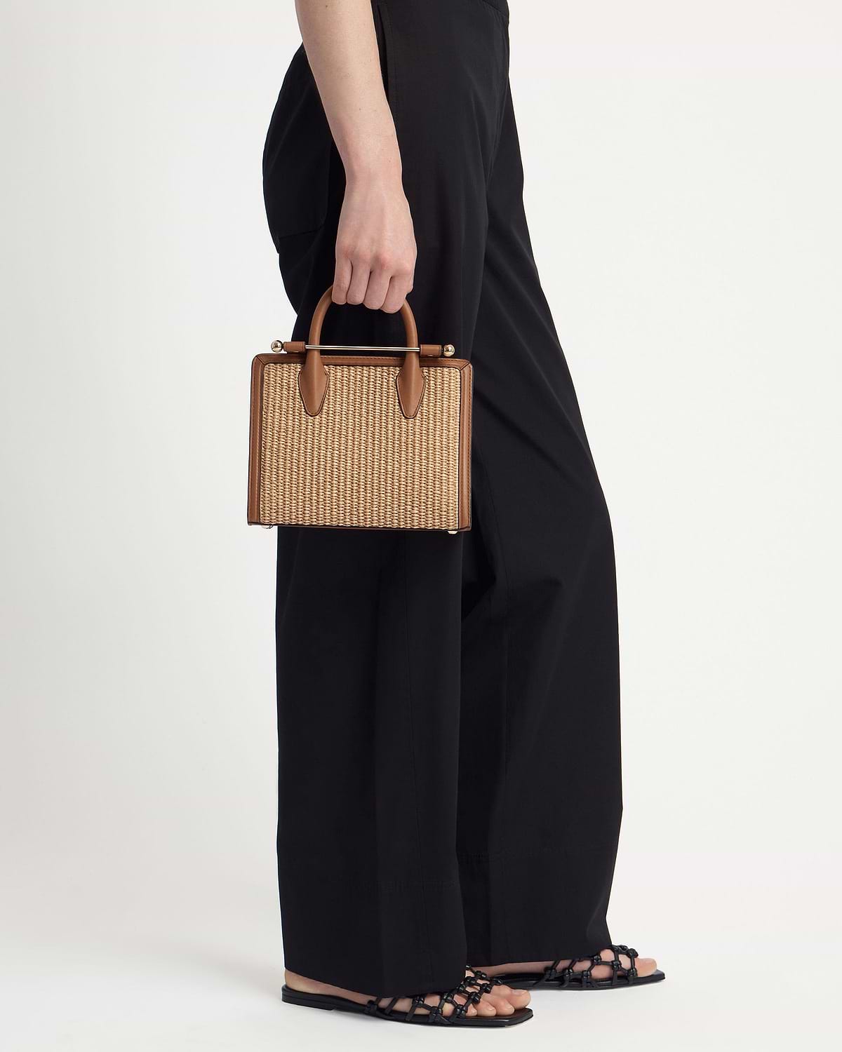 Mini tan raffia tote with leather trim and top handles held by model.