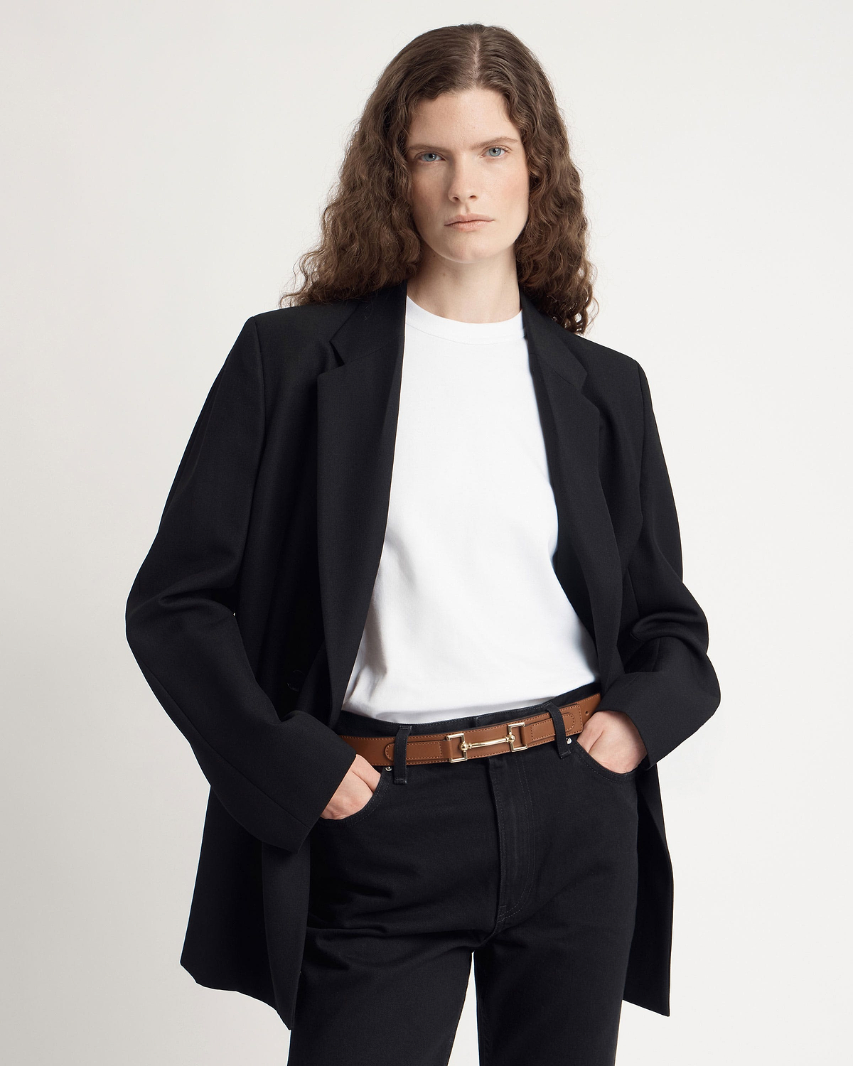 Model wearing a tan leather belt with gold hardware, black blazer and white t-shirt.