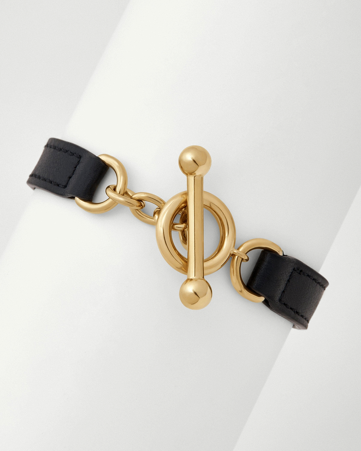 Close-up of black leather kite bracelet showing polished gold toggle clasp and chain.