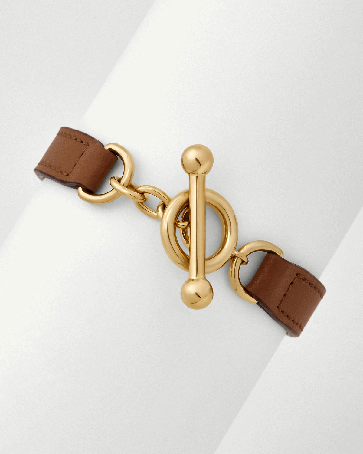 Tan leather kite bracelet with gold toggle clasp on white display.